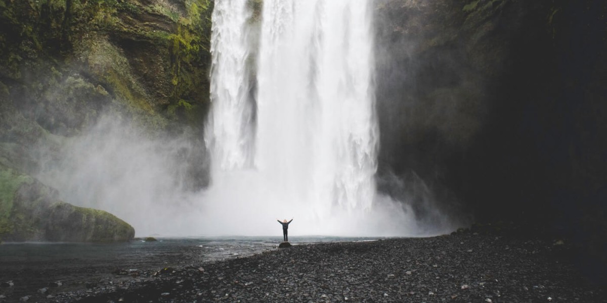 A huge waterfall in the background and a small figure standing at the bottom, raising their arms.